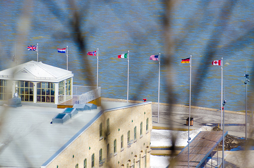 International flags floating besides St. Lawrence river from high angle point of view during day of springtime in Quebec city