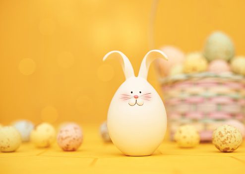 Cute Easter bunny in a vibrant yellow setting with a defocused Easter basket filled with speckled Easter eggs