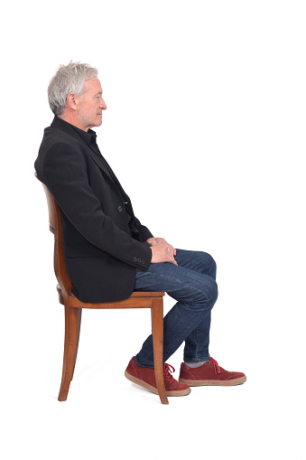 side view of a man sitting  on chair with sneakers jeans and blazer on white background