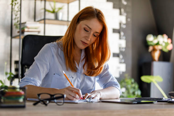 istock Diligent businesswoman sitting at her desk and writing work data on clipboard 1391463801