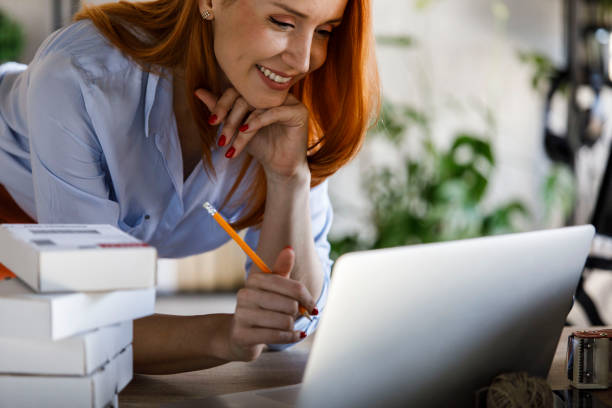 istock Smiling female entrepreneur surrounded with packages on her desk checking data on laptop 1391464105