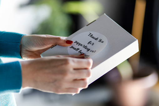 Close up shot of unrecognizable female entrepreneur applying a ''Thank you for supporting our small business'' label on a package.