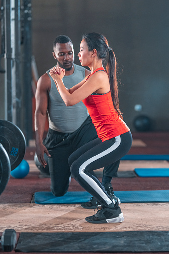 Male fitness instructor teaching exercise posture to sportswoman. Sportsman is training female athlete at gym. They are in sports clothing at health club.