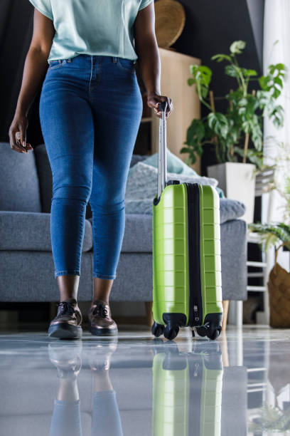 istock Young woman leaving for vacation, rolling a green suitcase by her side 1391468233