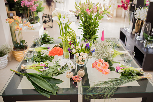 Woman puts vase with bouquet of flowers on table at home. Floral arrangement with orange roses. Interior and summer decor