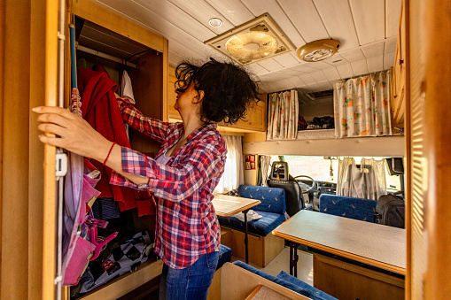 Mid-adult Caucasian woman, organizing her clothes into closet, in the camper van
