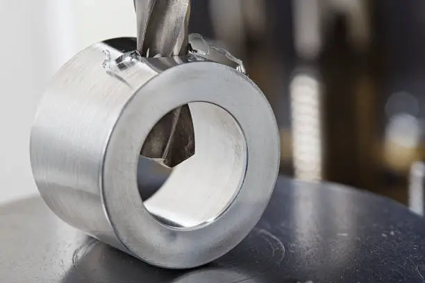 Photo of metal drill bit make holes in aluminium pipe on industrial drilling machine. Metal work industry.