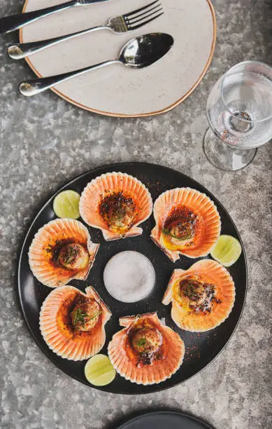 Scallops with flamed shells on a black plate. Luxury restaurant food. Seafood, selective focus. Fresh scallops flamed on a plate.