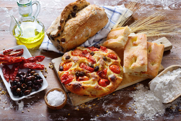 Focaccia barese with cherry tomatoes and olives. Olive bread, white focaccia, dried tomatoes and olives. Baked products on floured work surface. Typical ingredients and condiments of the Mediterranean diet. puglia stock pictures, royalty-free photos & images