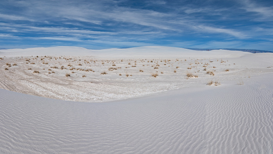 White Sands National Park covers 145,762 acres in the Tularosa Basin of the American Southwest.  The white dunes, largest of their kind on earth, are made up of gypsum sand dissolved from the surrounding mountains and carried into the basin almost 12,000 years ago.  In 1933 President Herbert Hoover designated the area as a national monument.  It became a national park in 2019.  These hikers on the sand dunes were photographed from the Alkali Flat Trail in White Sands National Park near Alamogordo, New Mexico, USA.