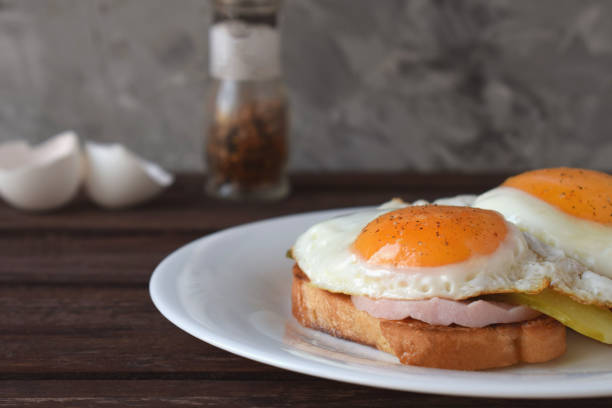 istock Fried eggs with liquid yolk on toasted bread with ham and pickles. 1391504330