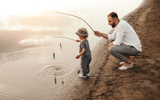 High angle of bearded man teaching boy to catch fish while playing on lake shore together