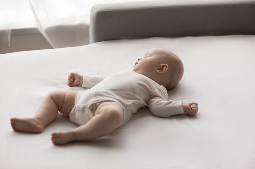 Peaceful carefree adorable little newborn baby boy girl in bodysuit sleeping on folded couch. Full length view of few months cute infant kid napping alone on cozy sofa, daily childcare routine concept