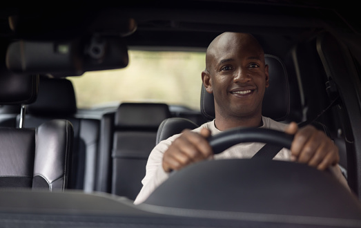 Portrait of a happy African American man driving a car and smiling - shot through windshield concepts