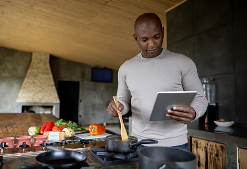 Happy African American man cooking at home following an online recipe on a tablet - domestic life concepts