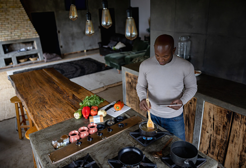 African American man cooking at home following a recipe on his tablet - domestic life concepts