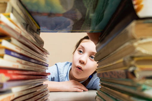 girl child with interest and curiosity examines stacks of books lying on reading, books,