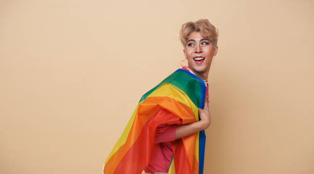 Youth asian transgender LGBT with Rainbow flag on shoulder isolated over nude color background. Man with a gay pride flag concept. stock photo