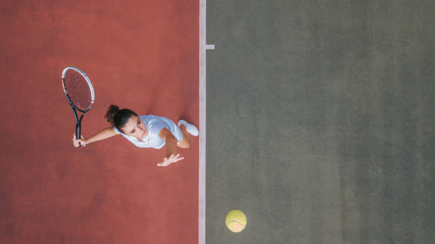 punto de vista de dron chica adolescente blanca jugador de tenis sirviendo la pelota practicando en la cancha de tenis directamente encima - deporte de raqueta fotografías e imágenes de stock