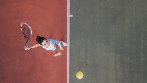 point de vue du drone adolescente blanche joueur de tennis servant la balle s’entraînant sur un court de tennis directement au-dessus - sport de raquette photos et images de collection