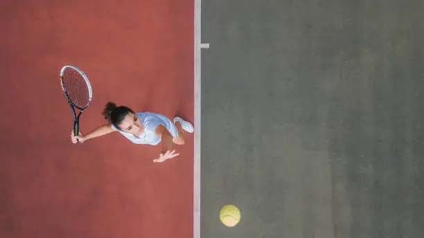 Photo of Drone point of view white teenage girl Tennis Player Serving The Ball practicing at tennis court directly above