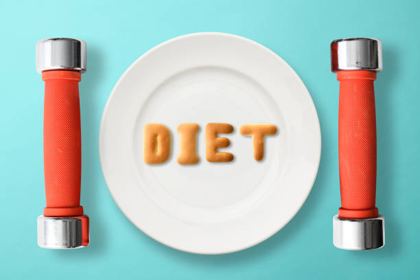 DIET letters written by cookies on white plate, with dumbbells on light blue background.\nDiet concepts.