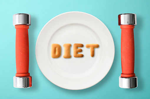 DIET letters written by cookies on white plate, with dumbbells on light blue background.
Diet concepts.