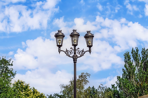 Decorative forged street lamp in Mykolaiv, Ukraine. Antique metal streetlight with three lamps close-up, isolated on blue sky background