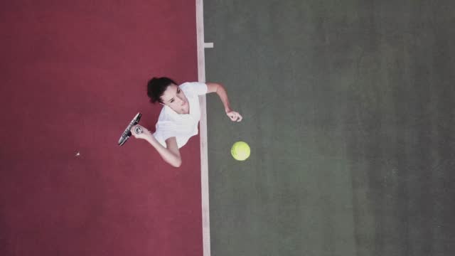 Drone point of view white teenage girl Tennis Player Serving The Ball practicing at tennis court directly above