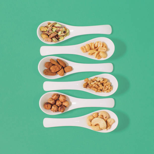 kernels of walnut, almond, hazelnut, cashew nut, peanut and pistachio in a ceramic spoons - nut directly above multi colored food imagens e fotografias de stock