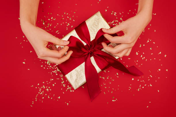 Hands tying a bow on a gift red background stock photo