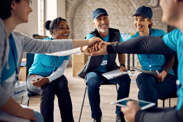 Team of motivated volunteers gathering hands in unity after successful meeting at donation center. Multiracial group of happy volunteers stacking their hands in unity while working at humanitarian aid center. community care stock pictures, royalty-free photos & images