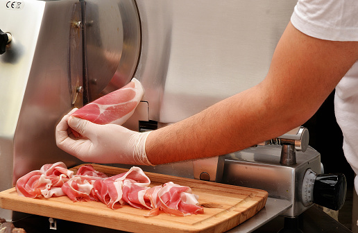 slicing prosciuto ham with industrial slicer machine.
