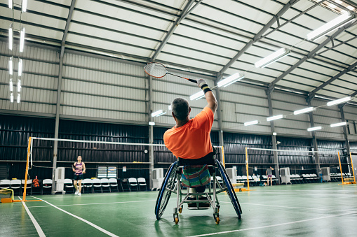 A senior man in an orange sportswear sits in a competitive wheelchair and enjoy badminton
