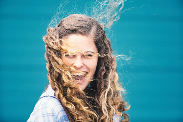 capelli ventosi da giorno: bella giovane donna dai capelli ricci ride mentre il vento avvolge i suoi lunghi capelli intorno al viso - untidy hair foto e immagini stock