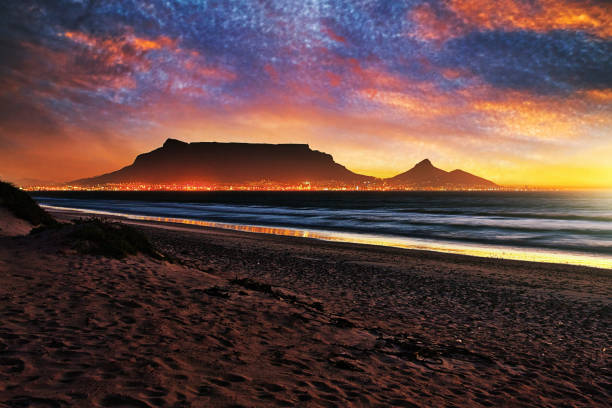 vue crépusculaire spectaculaire de montagne de table, le cap, l’afrique du sud à travers la baie de table avec la ville en feu avec la lumière - table mountain afrique du sud photos et images de collection