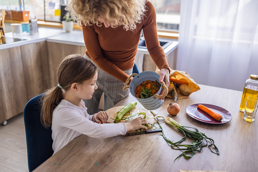 Caucasian mother and her daughter in the kitchen using leftovers from vegetable for compost