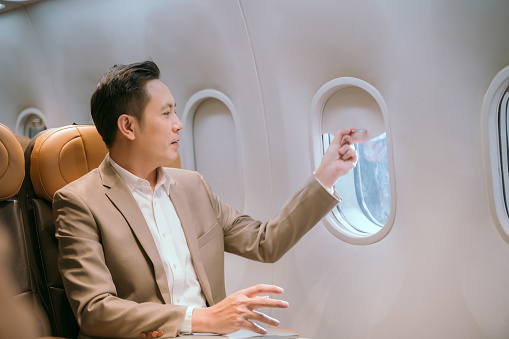 Asian businessman looks at the window on a plane while traveling abroad.