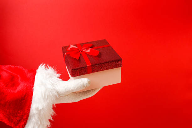 istock Santa Claus gloved hand holding giftbox on red background, copy space 1391574449