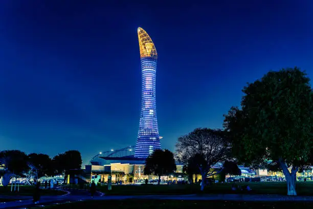 A huge building in the form of a torch located in the middle of a public park in the city of Doha, Qatar. View at night from a distance.