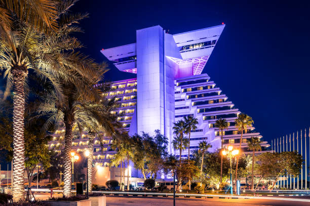 istock Modern building in downtown Doha, Qatar. View at night. The building is illuminated with a bright blue light against a dark night sky. A path with palm trees leads to the building. 1391576903