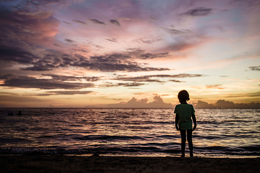 Back view of little boy standing on a beach at sunset. Copy space.