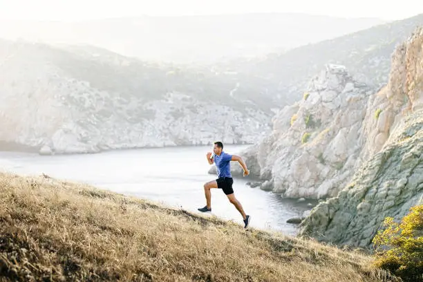 Photo of male runner running uphill in background sea bay