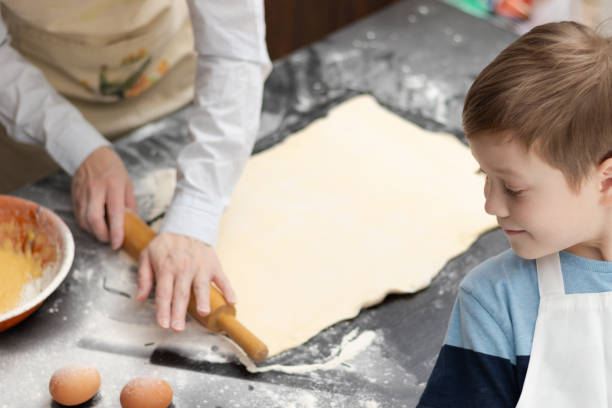 istock Mom and son in aprons roll out puff pastry for baking on a black kitchen table sprinkled with flour at home with a wooden rolling pin. Selective focus 1391580798