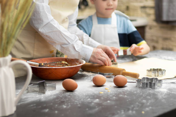 mãe e filho estão cortando moldes para assar biscoitos doces de massa folhada em uma mesa de madeira preta polvilhada com farinha em casa na cozinha. foco seletivo. - bread food baked 7 grain bread - fotografias e filmes do acervo