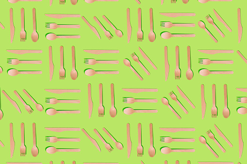 Seamless pattern made of fork spoon knife as cutlery made of natural material on bright green background. Minimal kitchen or ecology restaurant idea for zero waste concept. Template, menu cover design