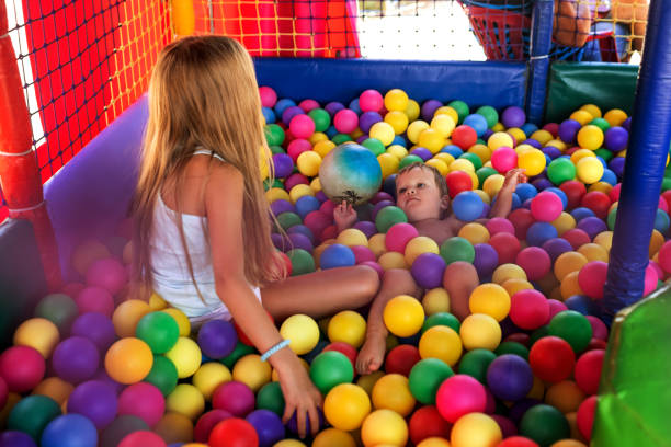 Cheerful beautiful bright older sister, is playing with her cute little cute little brother and throws colorful little balls at him while sitting in a small playroom