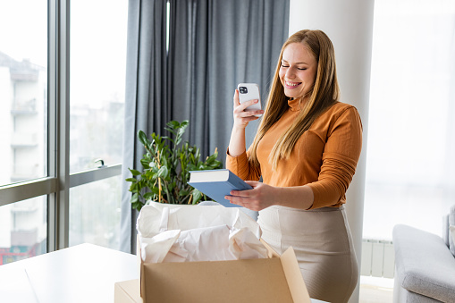 Young woman photo messaging her new online order to friends. She is using a smart phone.