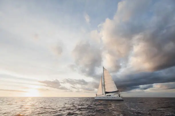 Photo of white yacht with sail set goes along the island on a hot day. blue sea, blue sky. on board a young couple in love. the bride and groom. wedding boat trip.