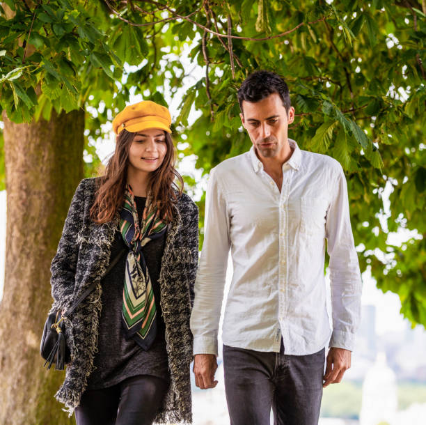 A couple in discussion as they walk in a London park during summer.